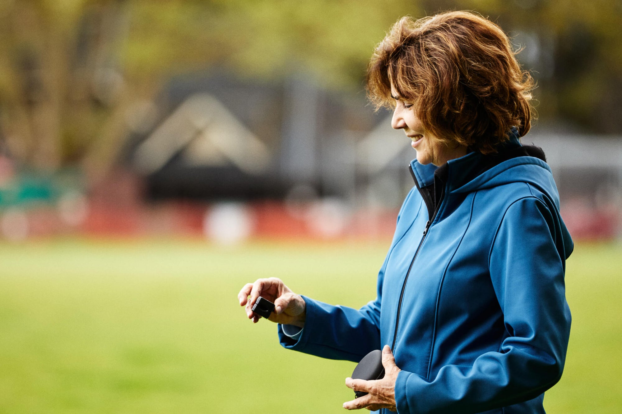 Woman wearing blue jacket smiling using iHeart device