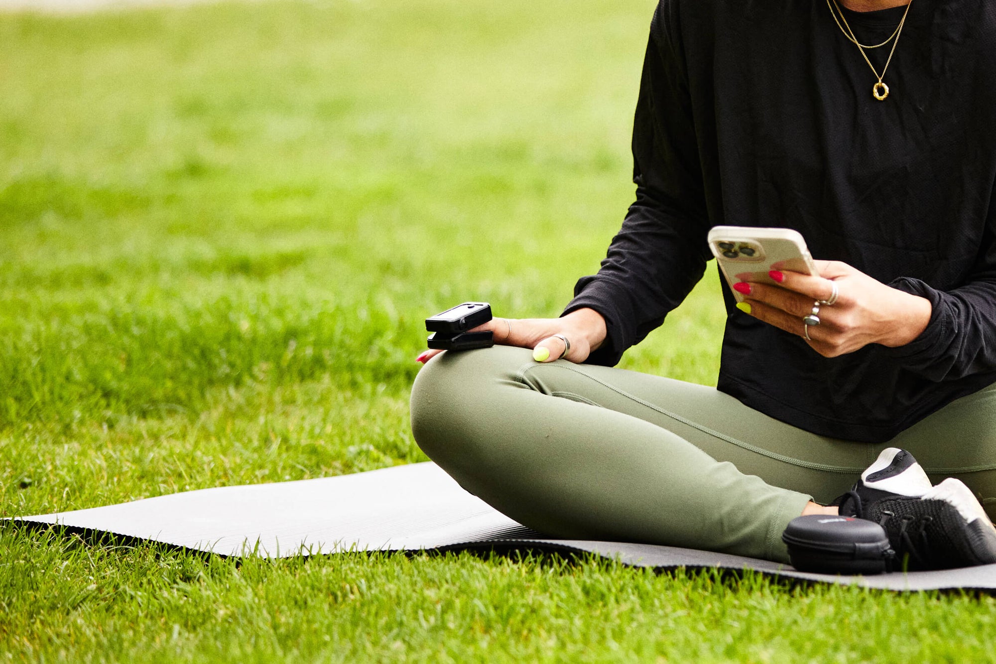 Female sitting on green grass, using smartphone with the iHeart device